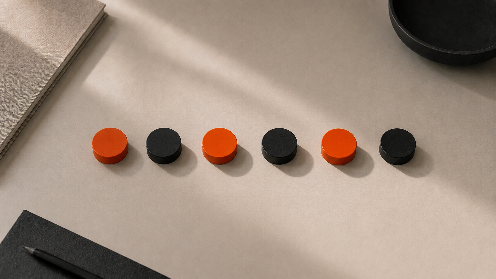 Sechs runde Objekte in einer Reihe auf hellem Untergrund, abwechselnd orange und schwarz