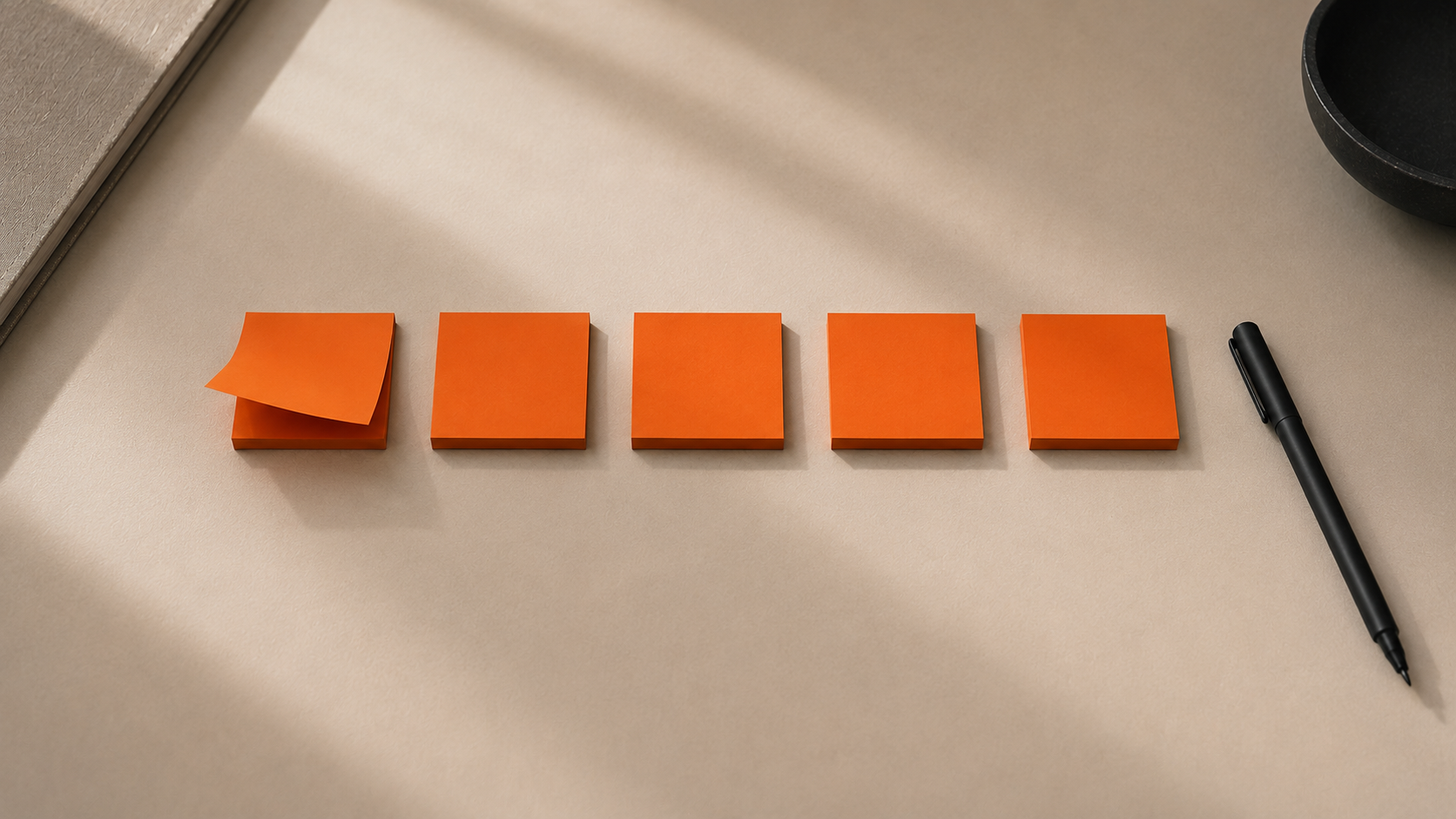 Fünf orangefarbene Haftnotizen in einer Reihe neben einem schwarzen Stift