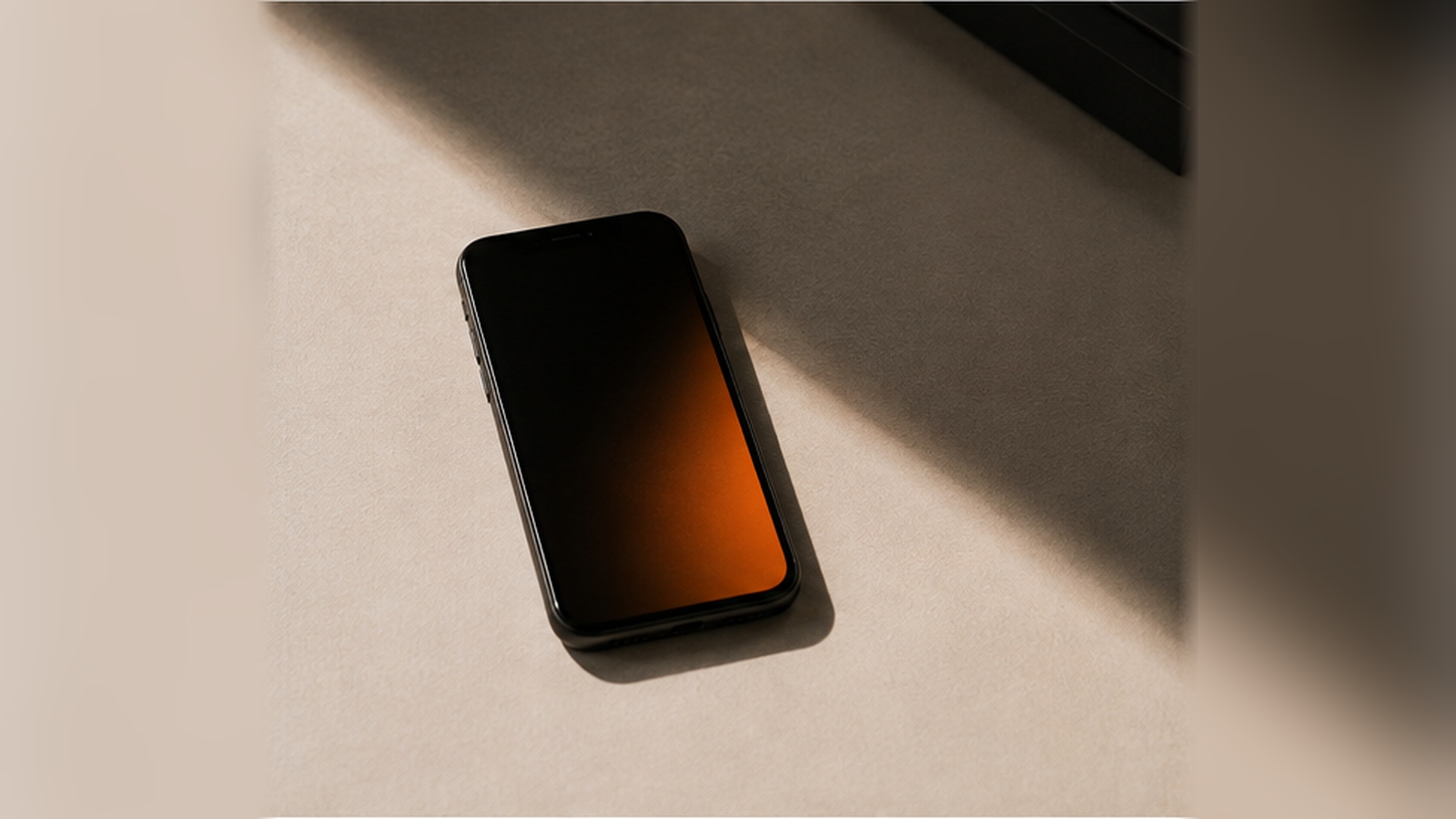 Schwarzes Smartphone halb im Schlagschatten, mit warmem orangem Lichtschein auf dem Display